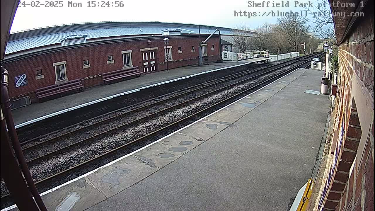 A view of a train platform on an overcast day, showing railway tracks, a brick building, and benches.