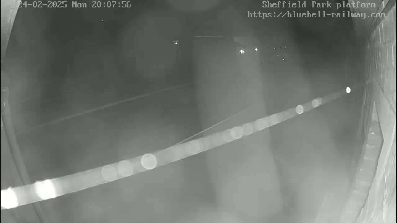 A nighttime, low-light security camera view shows a dark platform area with faint lights in the distance.