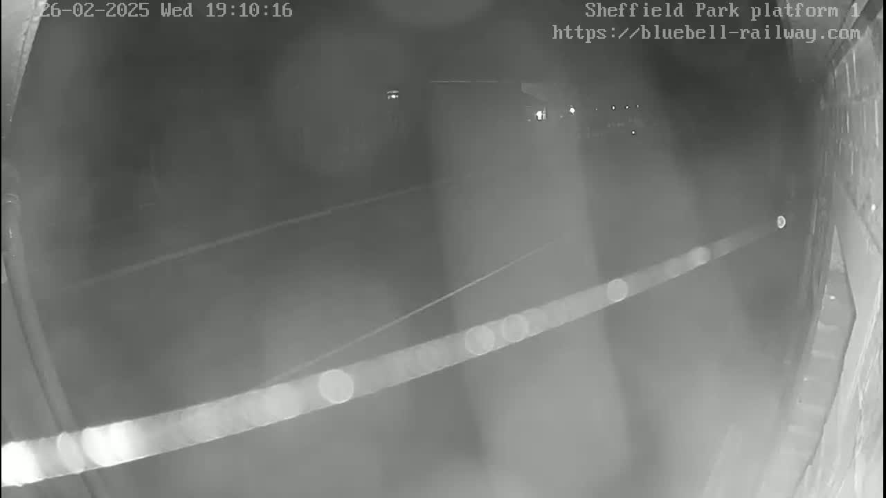 A nighttime, low-light security camera image shows a dark, empty train platform.