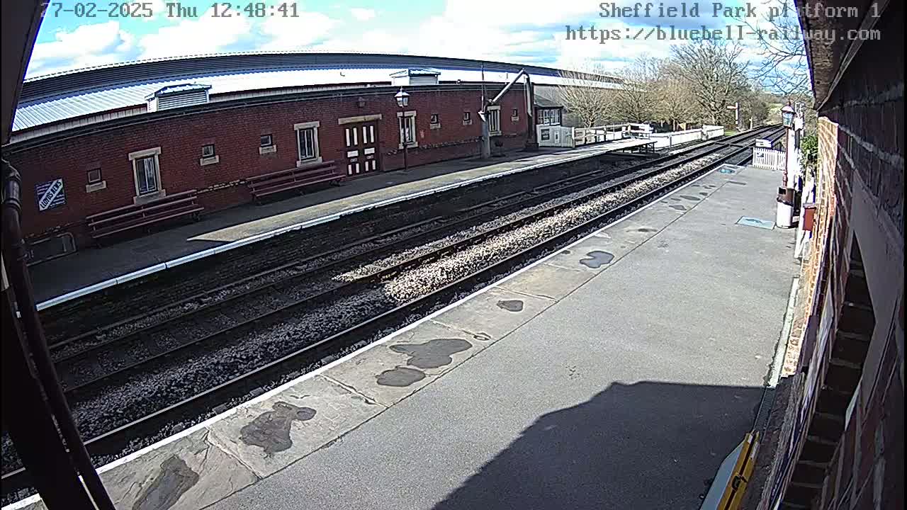 A train platform with two sets of tracks under a partly sunny sky.