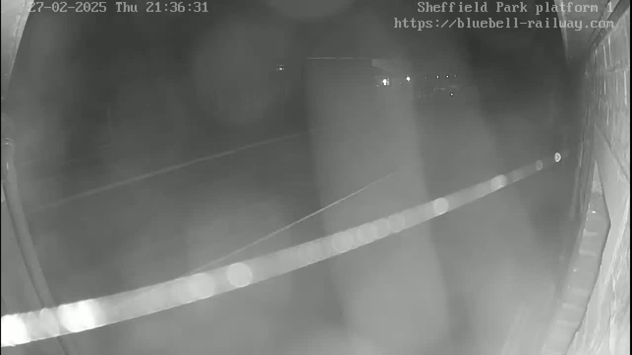 A nighttime, low-light security camera view shows a dark, empty platform with a faint light source in the distance.