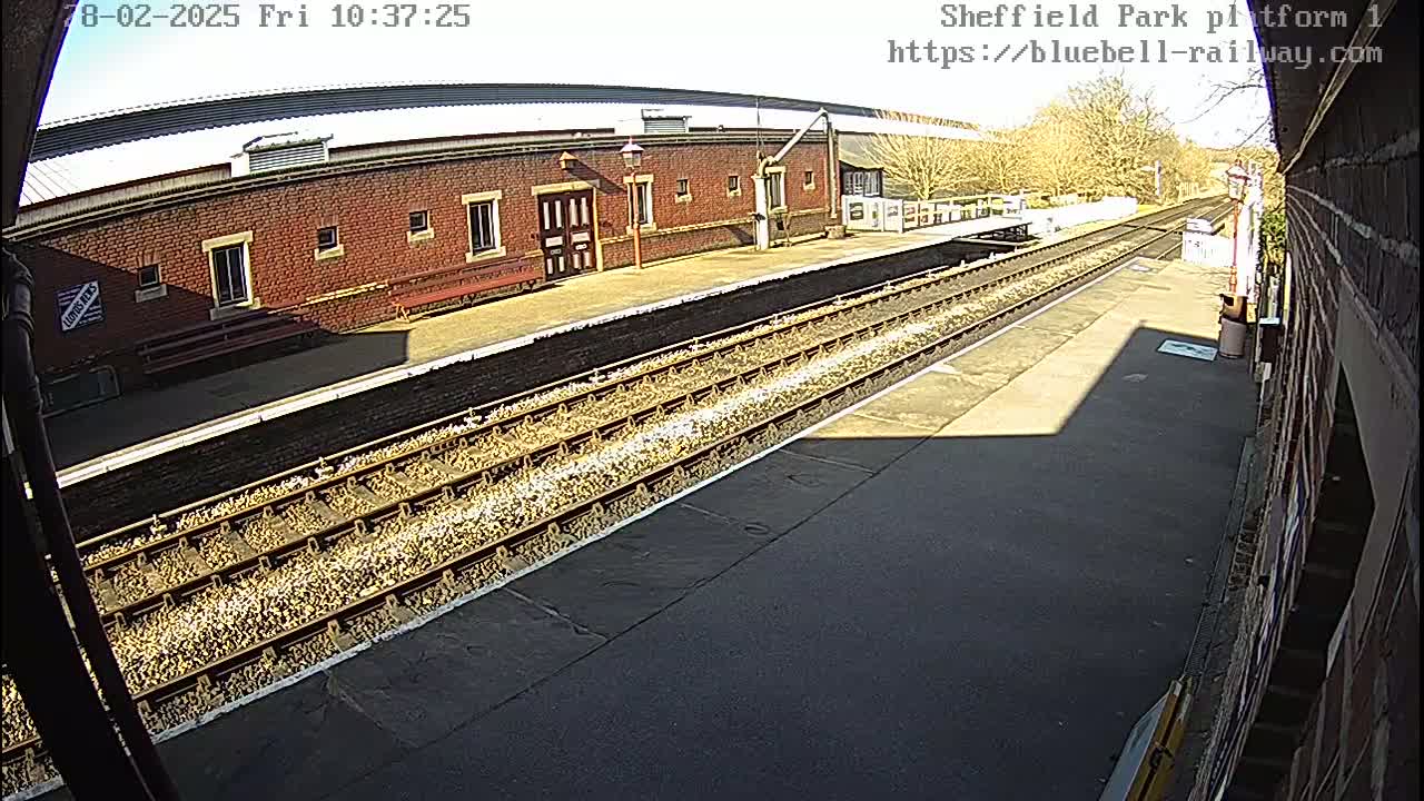 A sunny view of a train platform with a brick building and multiple train tracks.