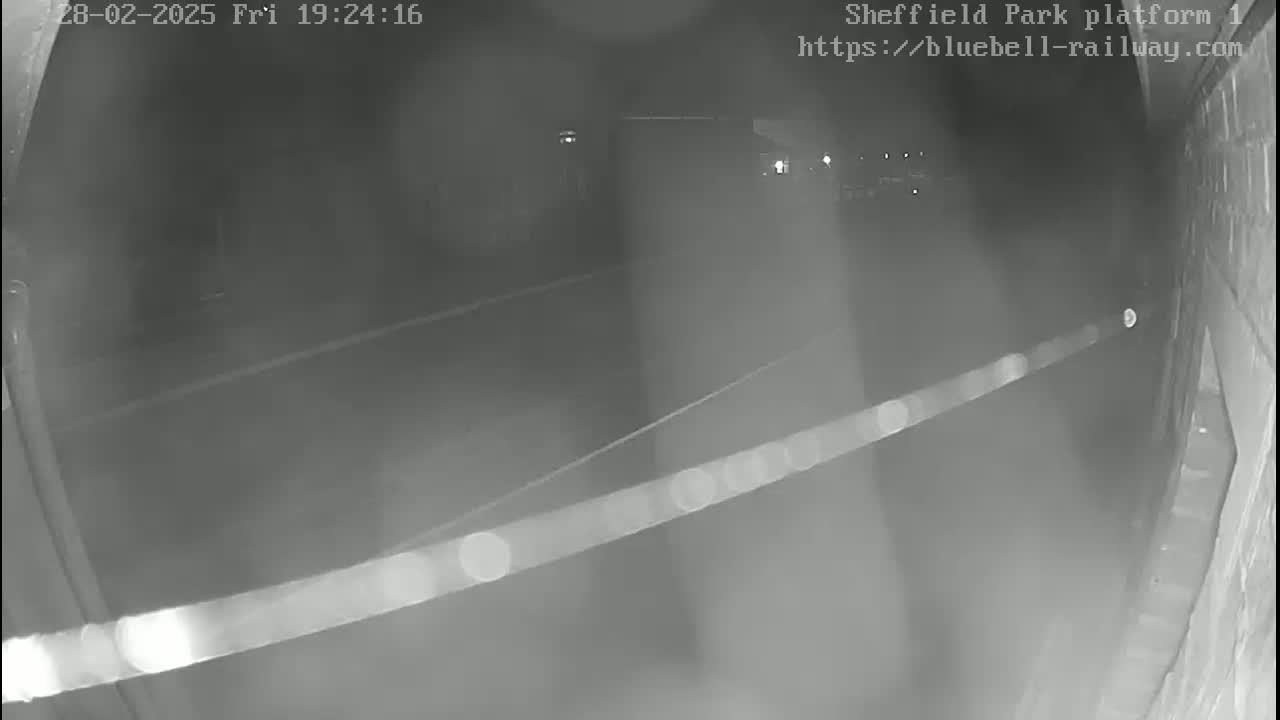 A nighttime, low-light security camera view shows a dark, empty platform area with a faint light source in the distance.