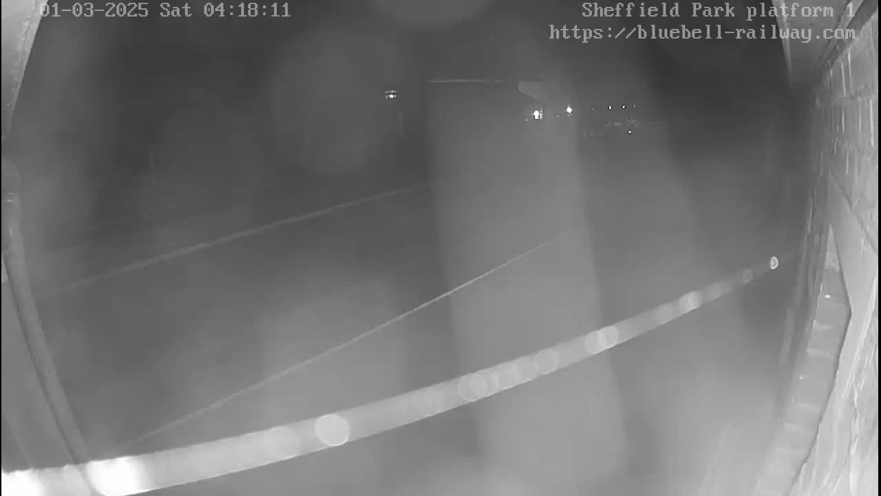A nighttime, low-light security camera view shows a dimly lit empty platform or roadway.