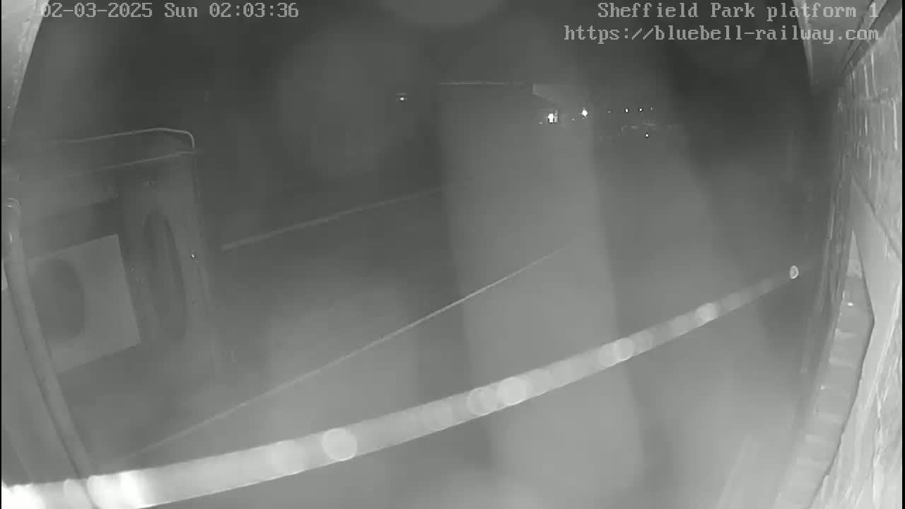 A nighttime low-light security camera image shows a mostly empty platform area at a train station.