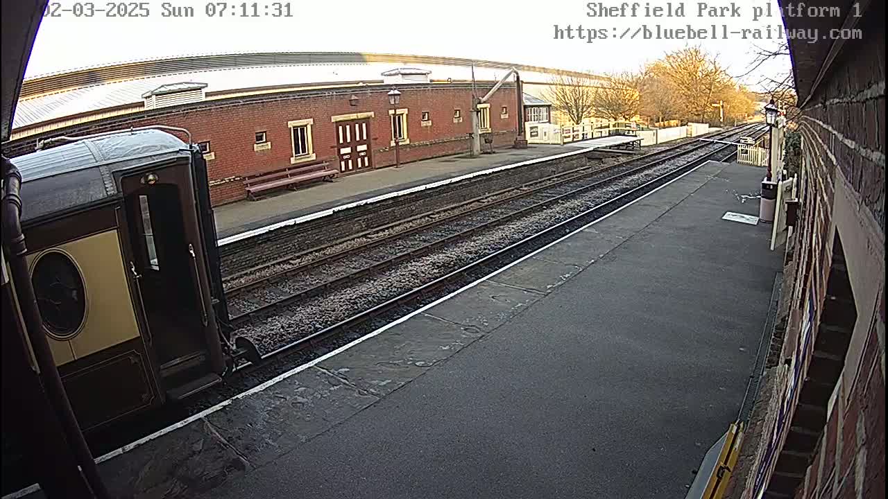 A train car is stopped at a railway platform on a partly sunny day.