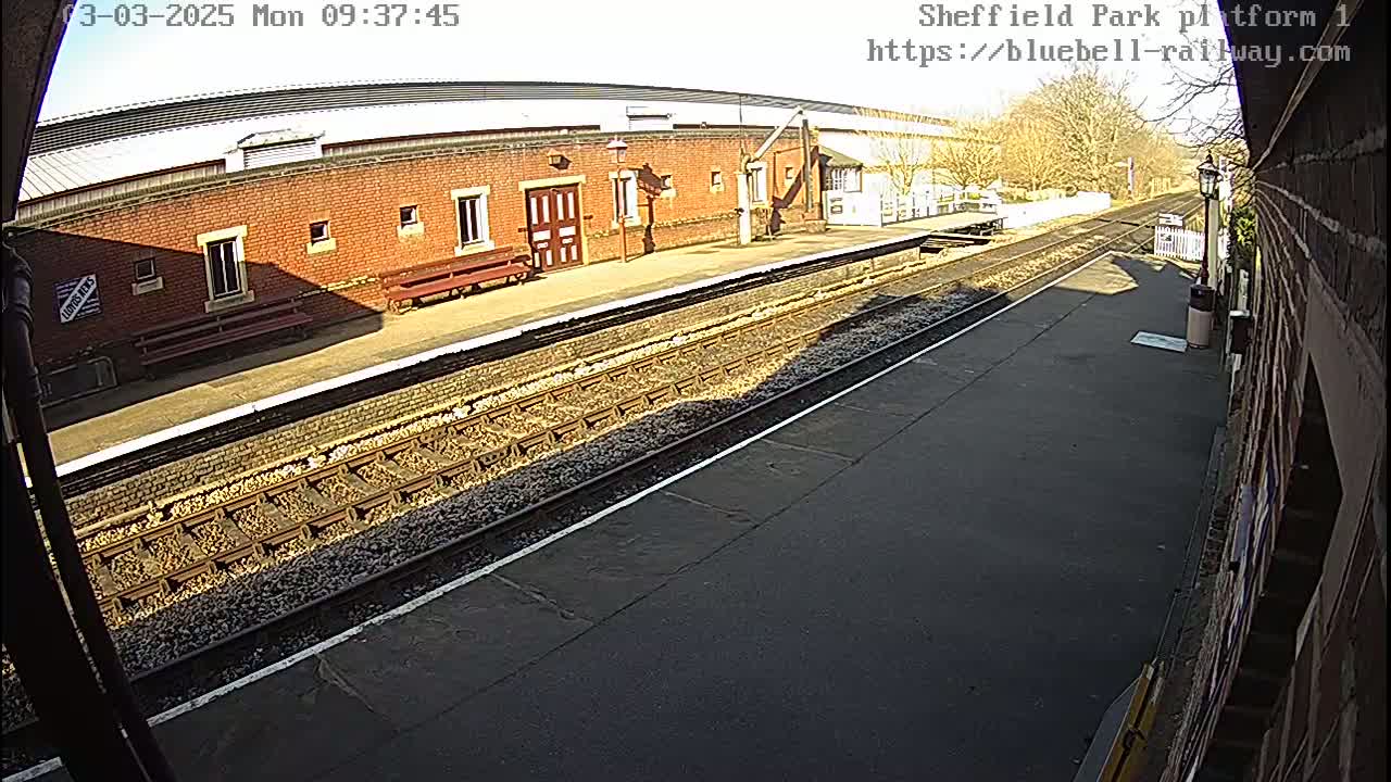 A sunny view of a train platform with a brick building and train tracks.