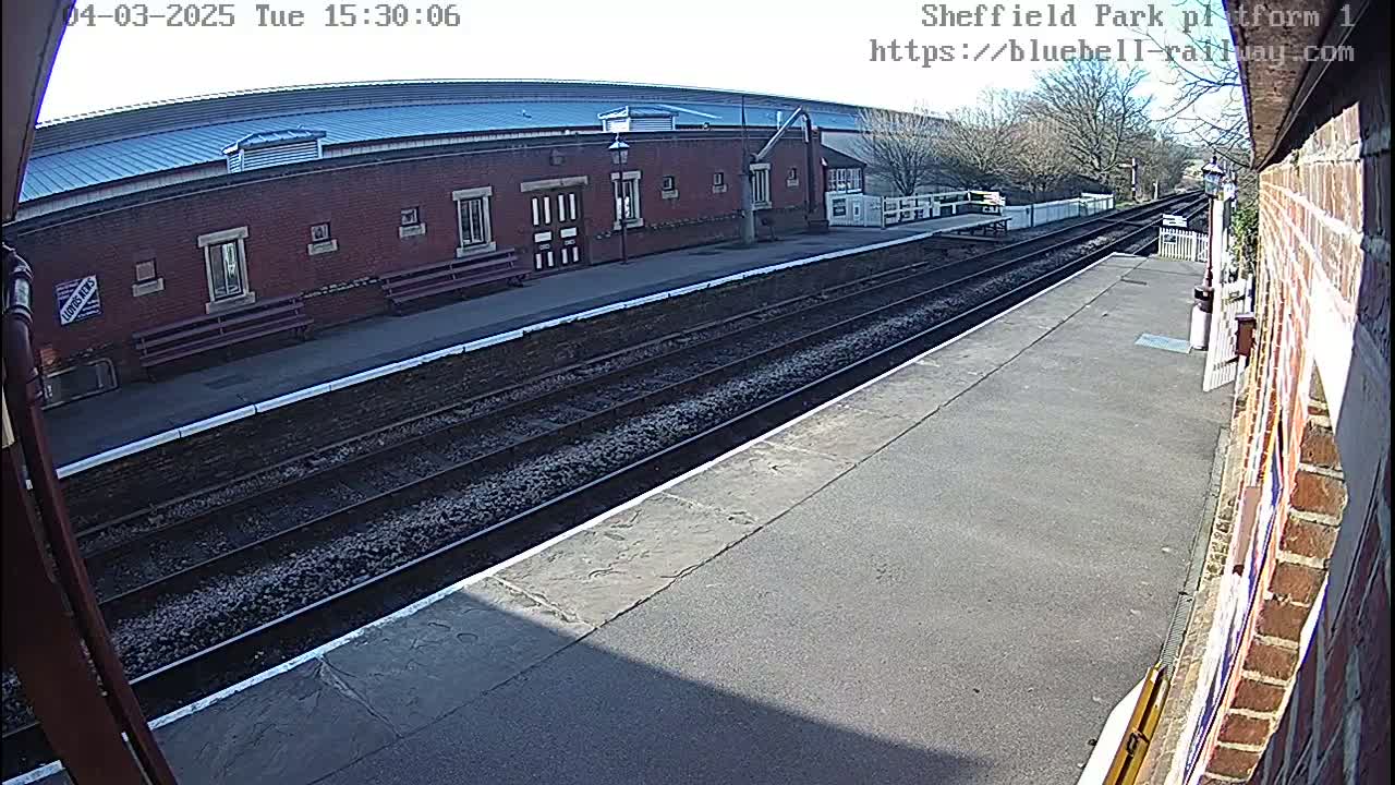 A train platform with multiple train tracks and a brick building in the background on a sunny day.