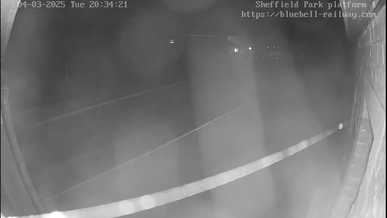 A nighttime, low-light view of a dark platform area with faint markings on the ground, possibly a railway platform.
