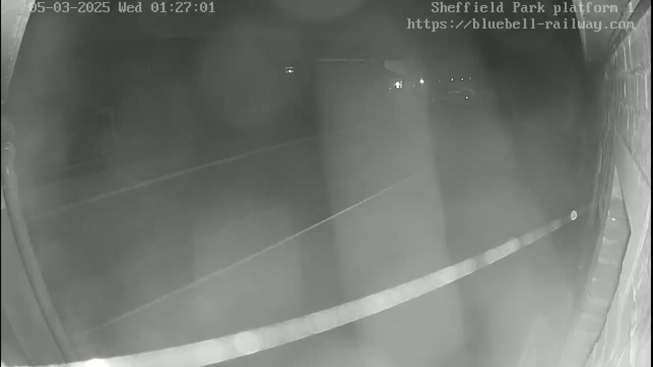 A nighttime, low-light view of a dark platform or roadway shows faint markings on the ground, and a wall is visible to the right.