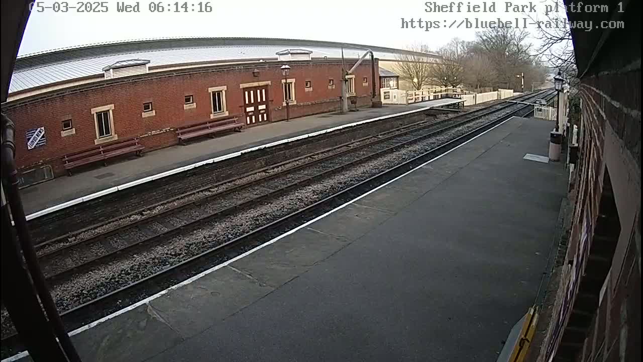A train platform with a brick building and train tracks under an overcast sky.