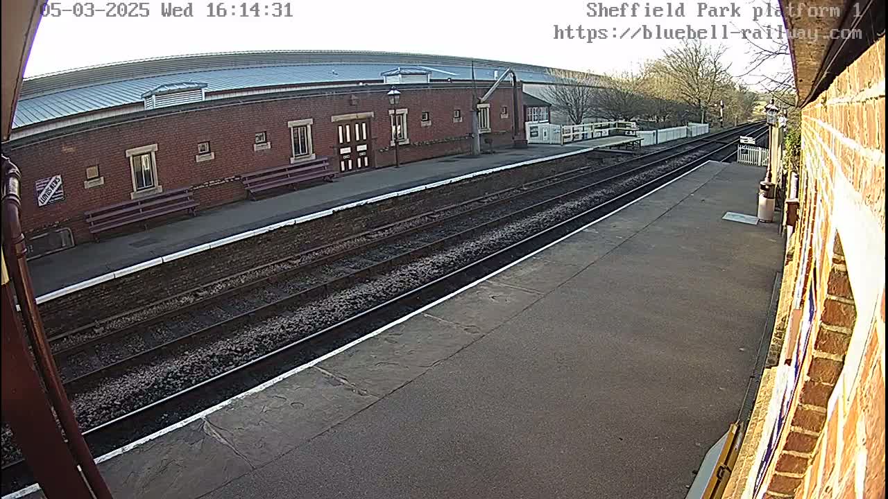 A train platform with a brick building and train tracks under a clear sky.