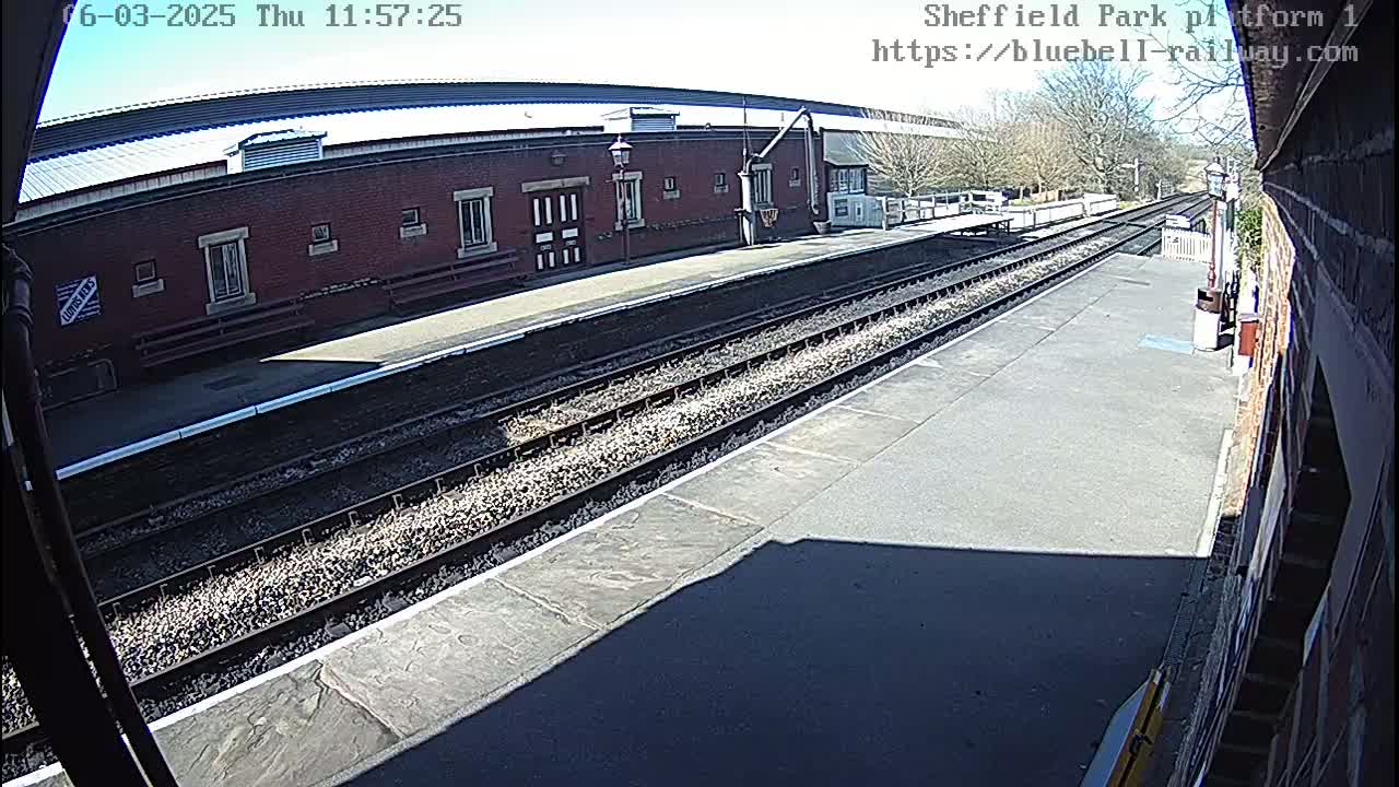 A sunny view of a train platform with two parallel train tracks extending into the distance, beside a brick building.