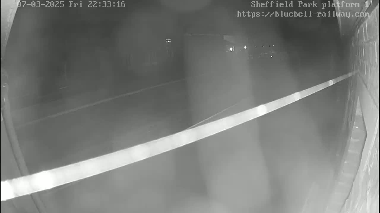 A nighttime, low-light security camera view shows a dark, empty platform area with a bright horizontal line crossing the frame.