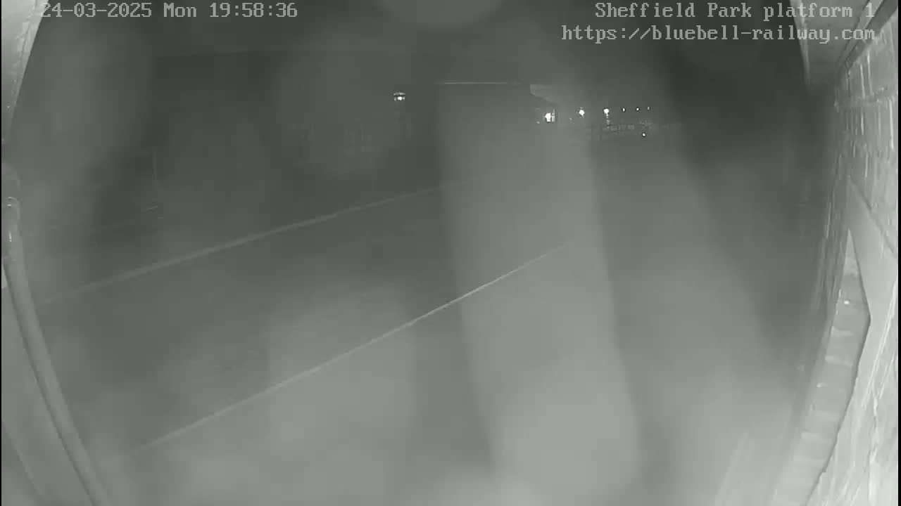 A nighttime, low-light view shows a dark roadway or platform with faint markings and indistinct shapes in the distance.