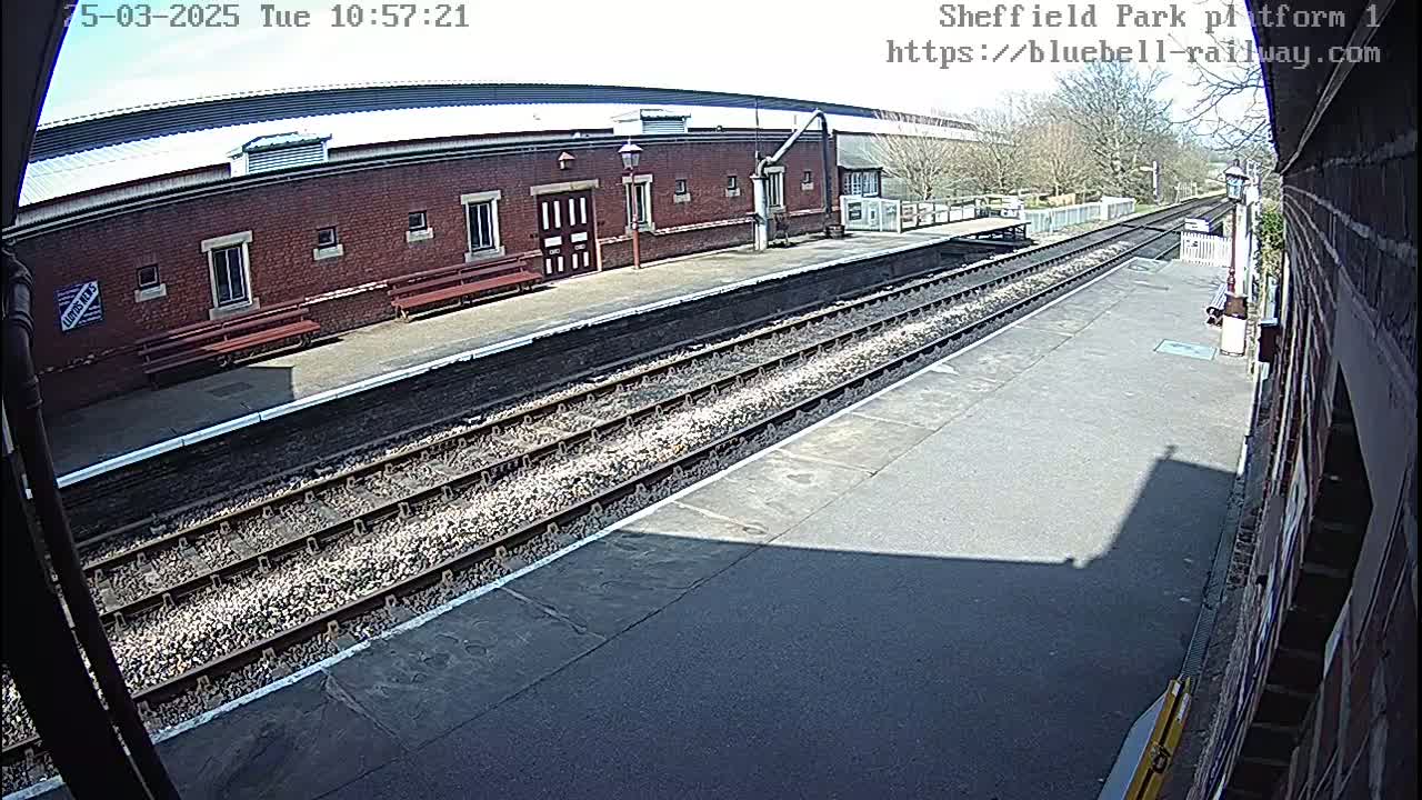 A sunny view of a train platform with a brick building and train tracks.
