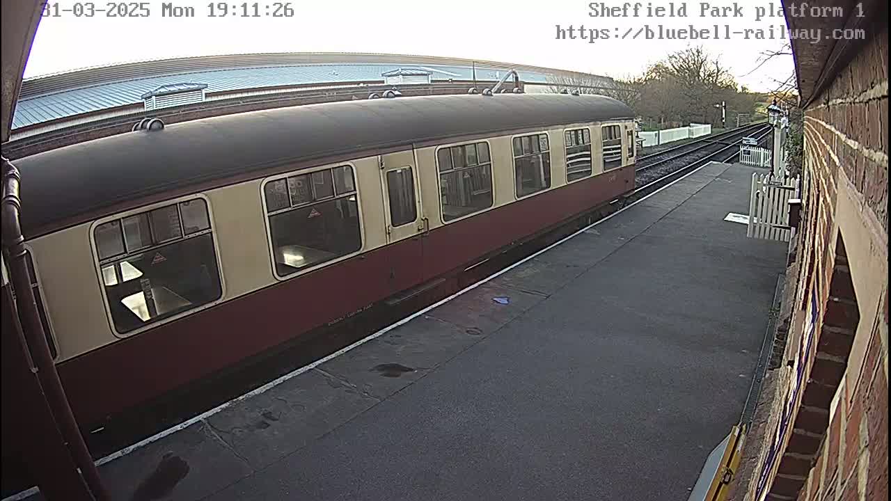 A maroon and cream passenger train is stopped at a railway platform on a partly sunny day.
