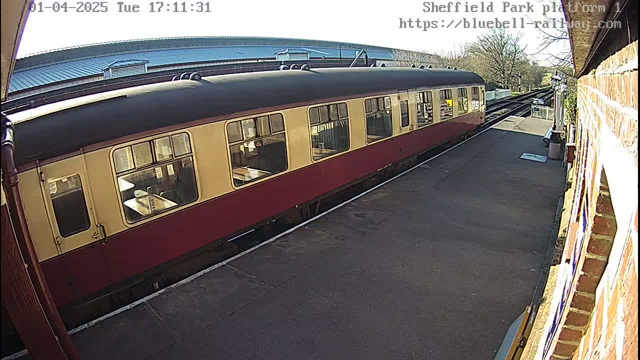 A maroon and cream passenger train is parked at a station platform on a sunny day.