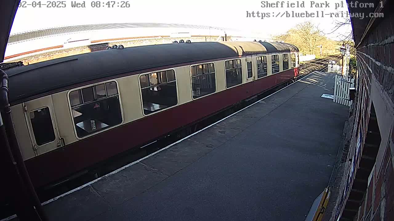 A maroon and cream passenger train car sits at a station platform on a sunny day.