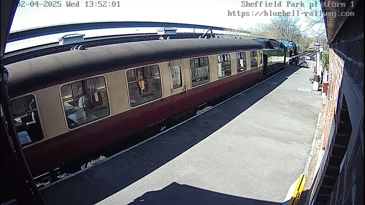 A maroon and cream passenger train is at a station on a sunny day.