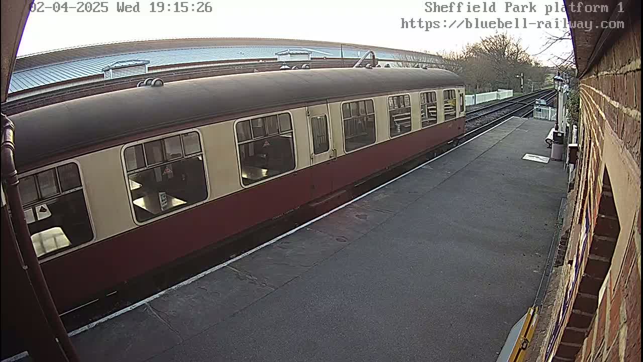 A maroon and cream passenger train is stopped at a station platform on an overcast day.