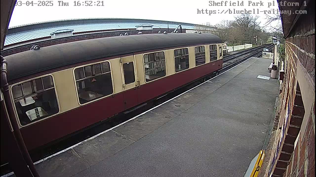 A maroon and cream railway carriage is parked at a station platform on an overcast day.