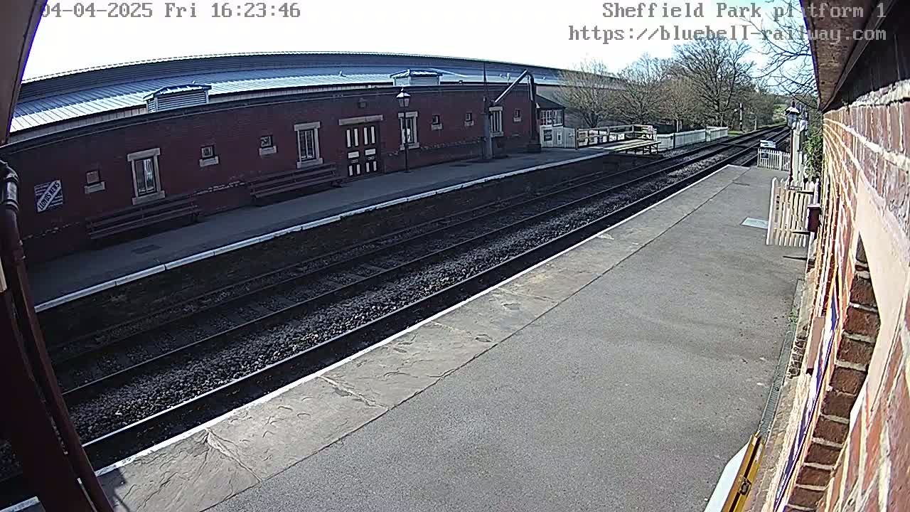 A view of a train platform on a sunny day shows train tracks leading to a brick building.