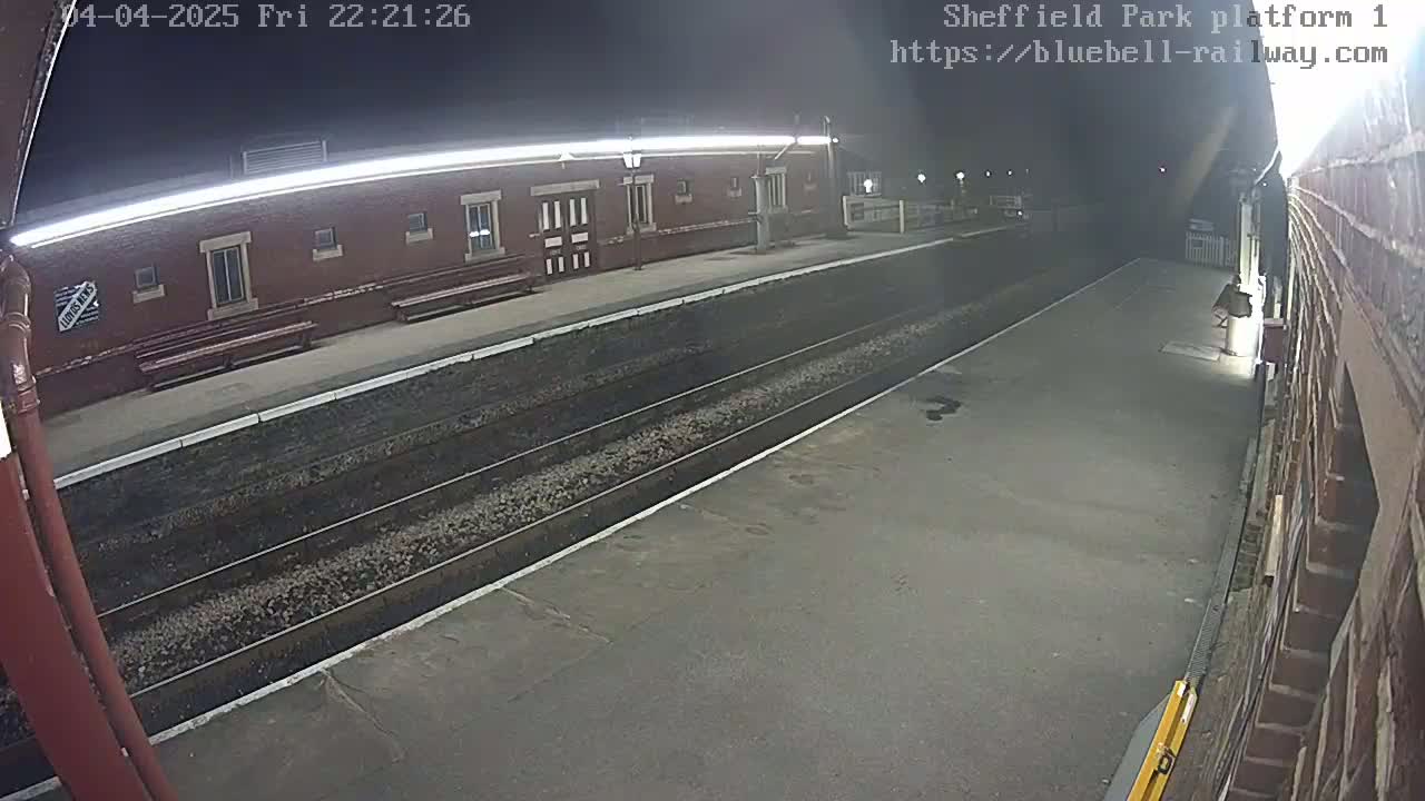 A nighttime view of a deserted train platform with two train tracks and a brick building under a clear, dark sky.