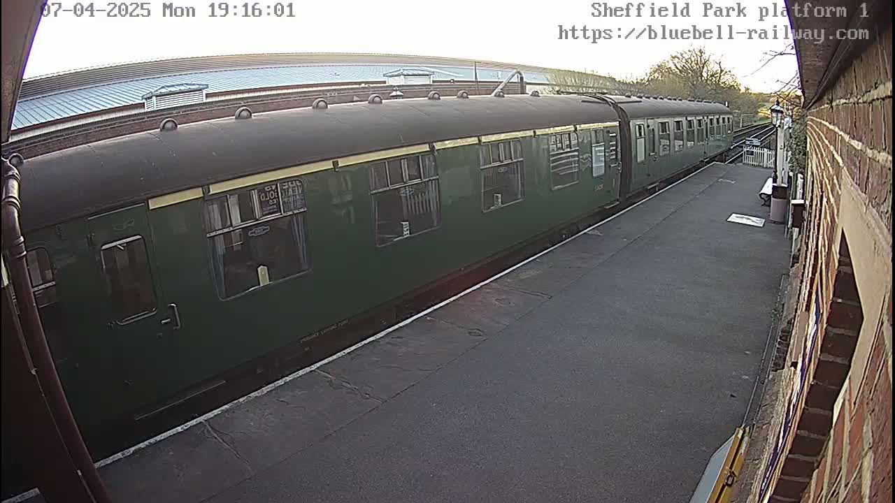 A dark-green passenger train sits at a station platform on an overcast day.