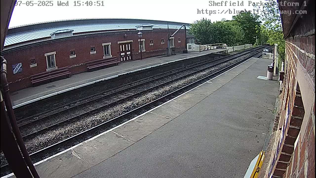 A mostly sunny view of a train platform with two sets of tracks and a brick building.