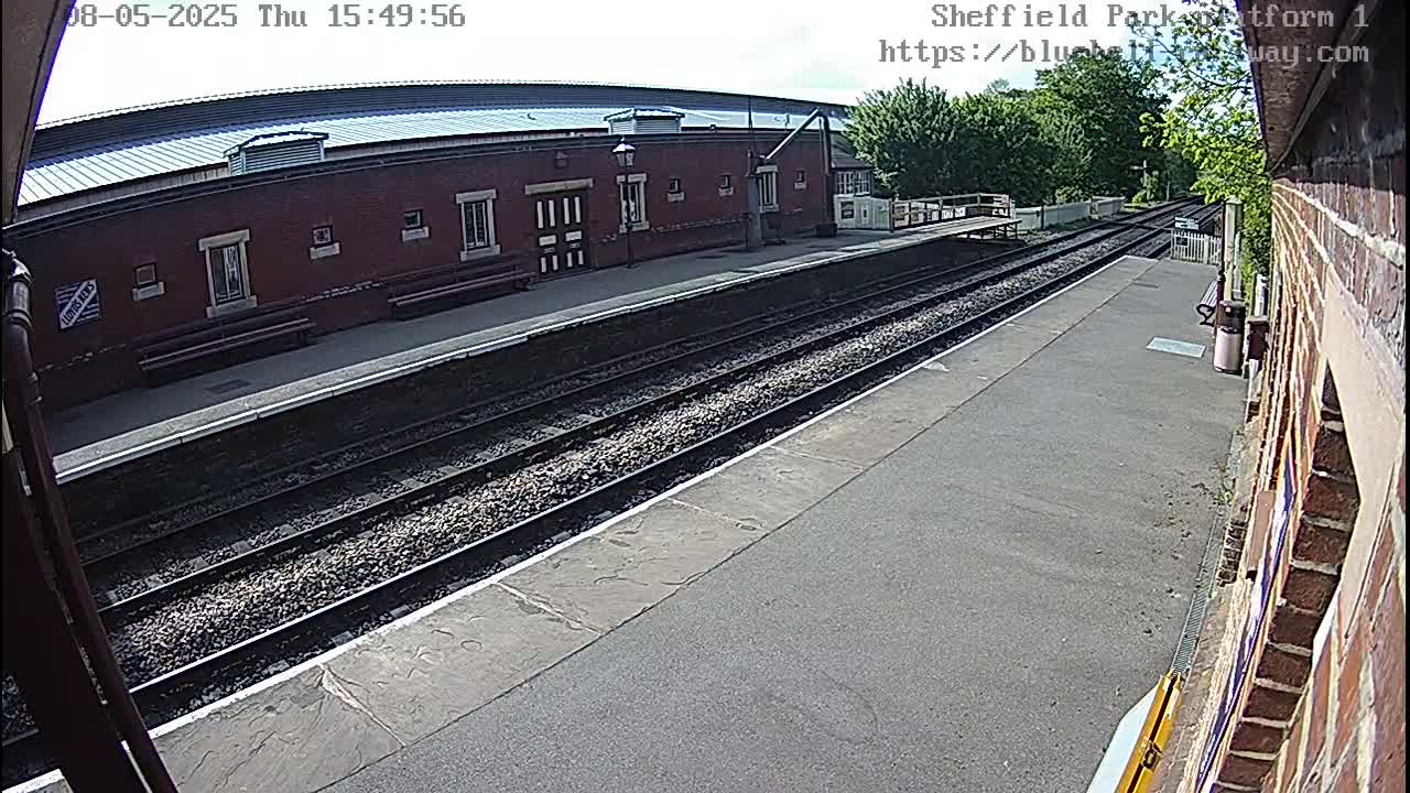 A train platform with two sets of tracks and a brick building under a partly cloudy sky.