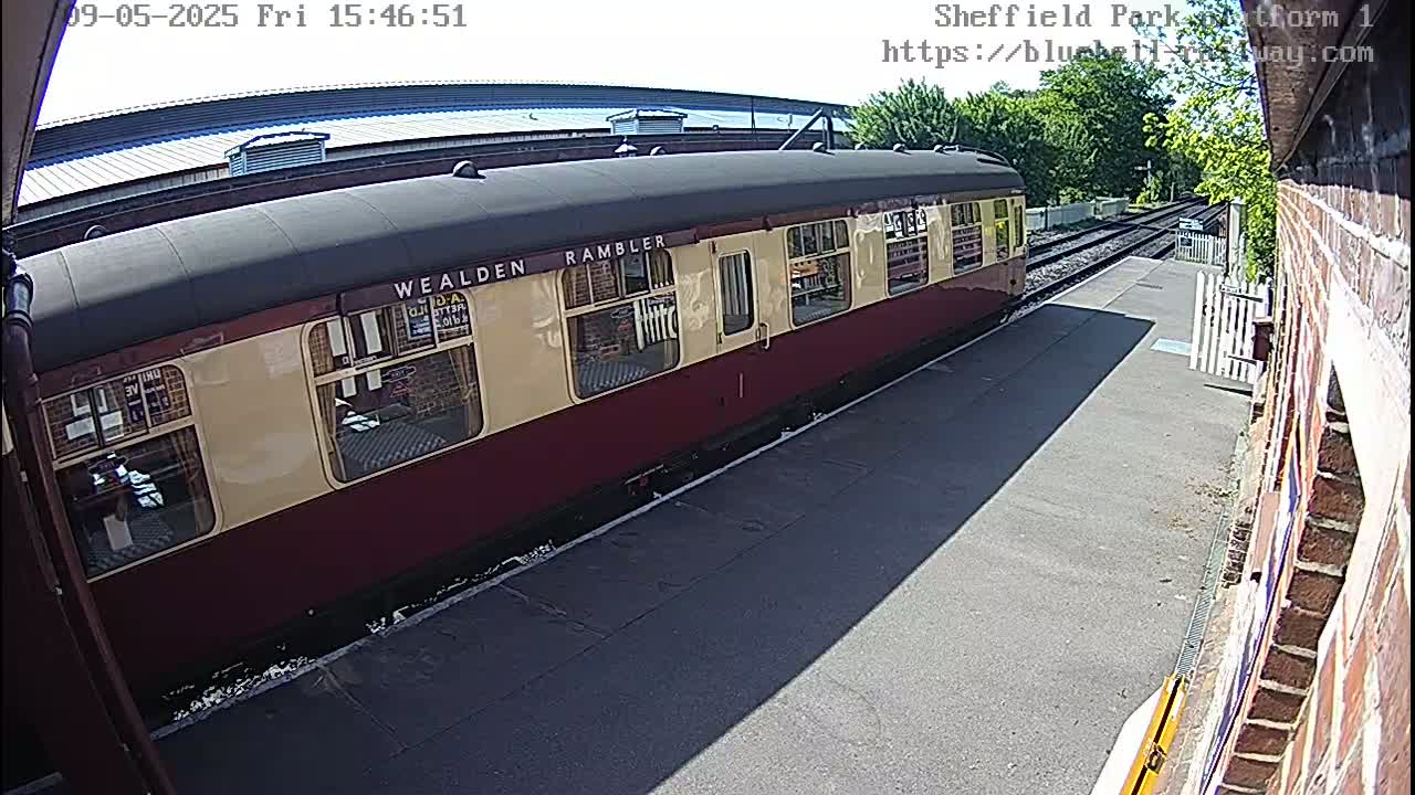 A maroon and cream passenger train car sits at a station platform on a sunny day.