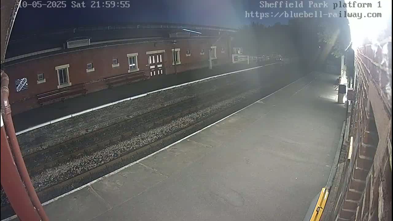 A nighttime view of an empty train platform with a brick building and train tracks.