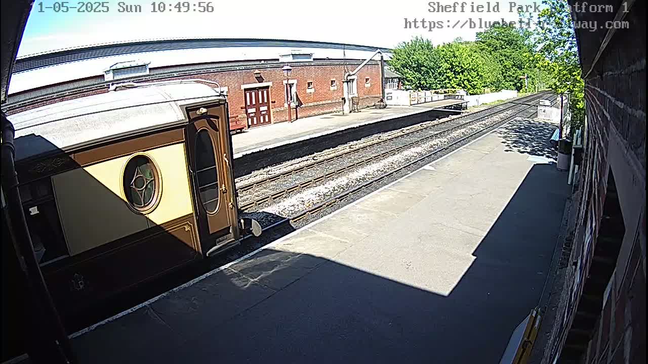 A luxury train car is parked at a sunny train station platform next to train tracks.