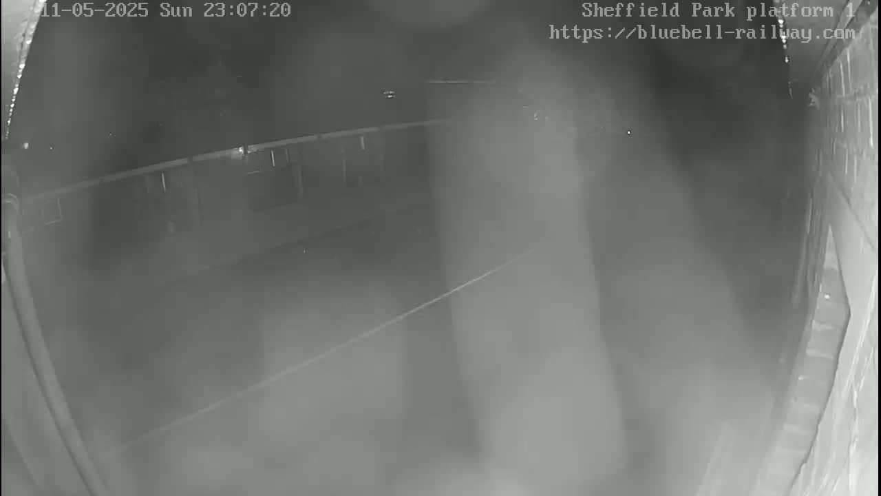 A nighttime, low-light security camera image shows a mostly empty platform with a faintly visible structure in the background.