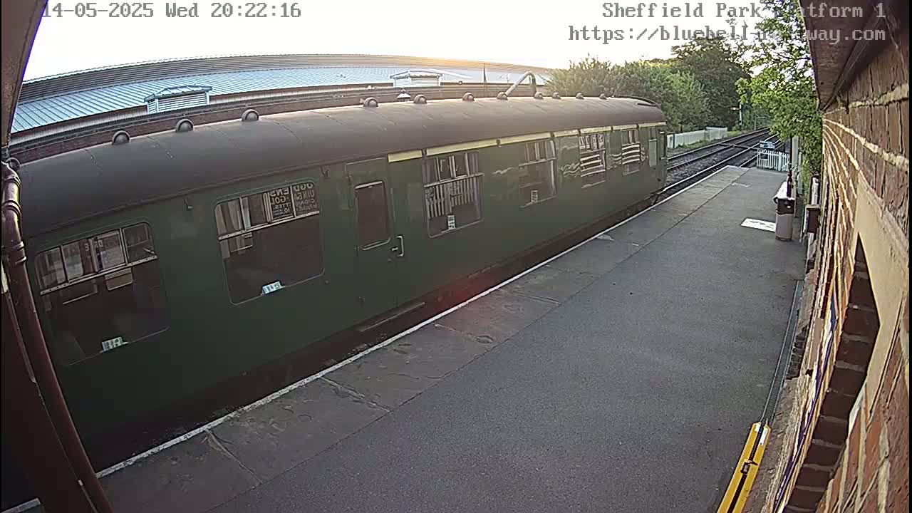 A dark-green passenger train is parked at a station platform in the evening light.
