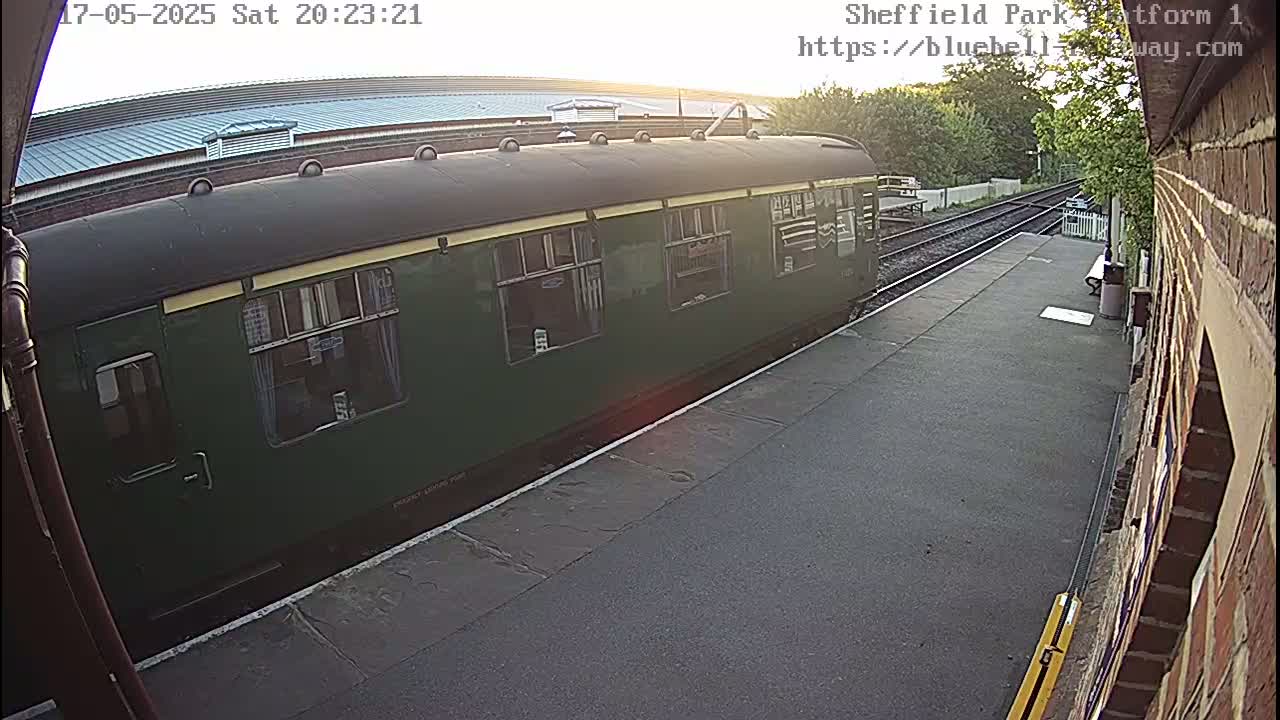A dark green passenger train is at a station platform on a partly sunny evening.