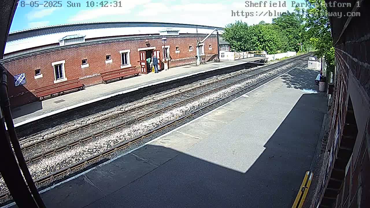 A sunny view of a train platform with a brick building and train tracks.