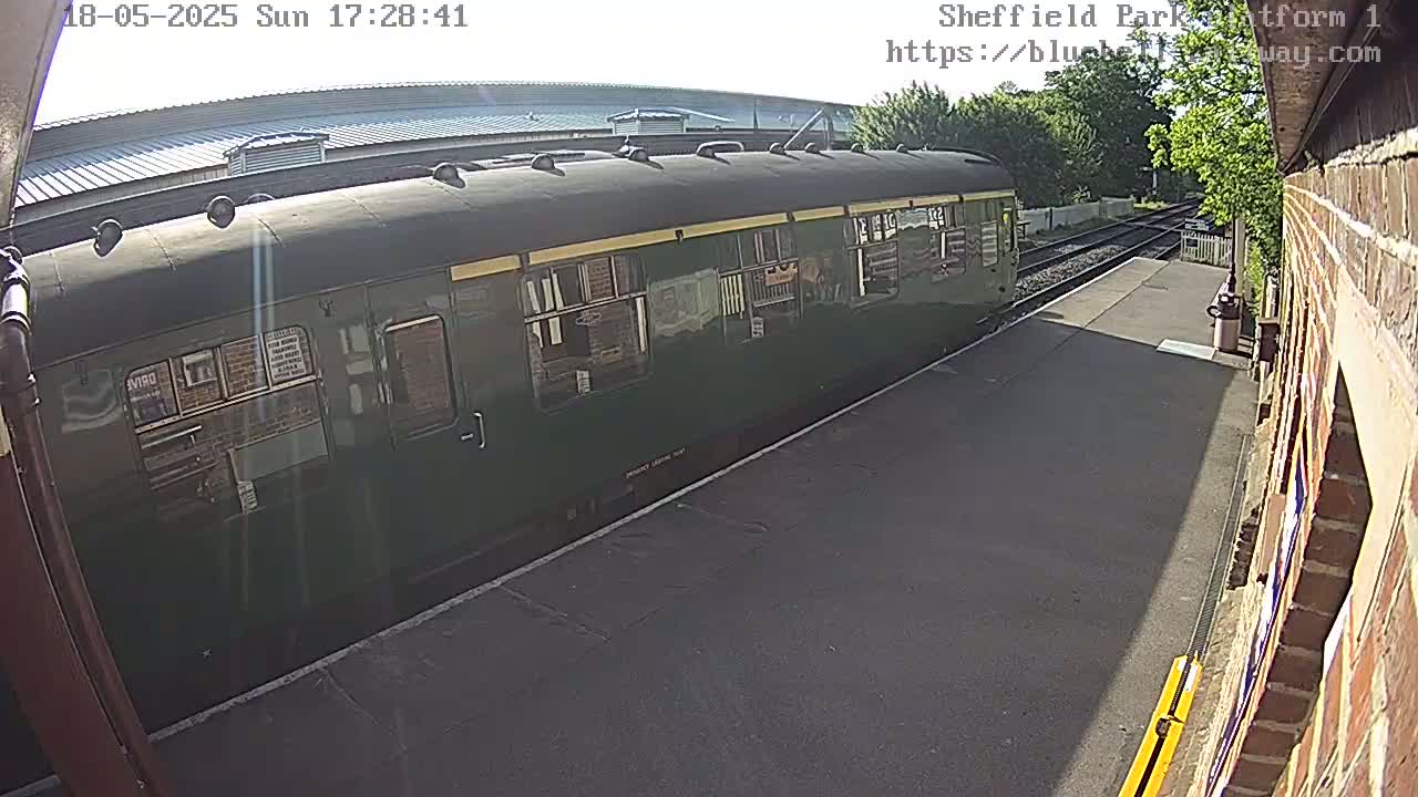 A dark-green passenger train is at a station on a sunny day.