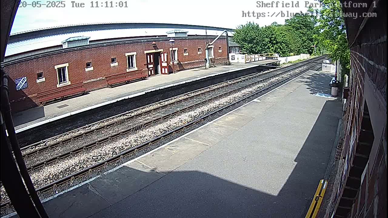 A sunny view of a train platform with a brick building and train tracks.
