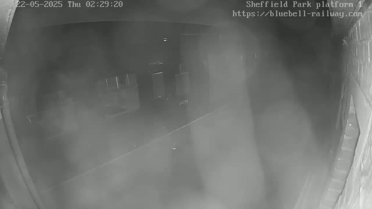 A dimly lit, foggy train platform is seen at night from a low angle.