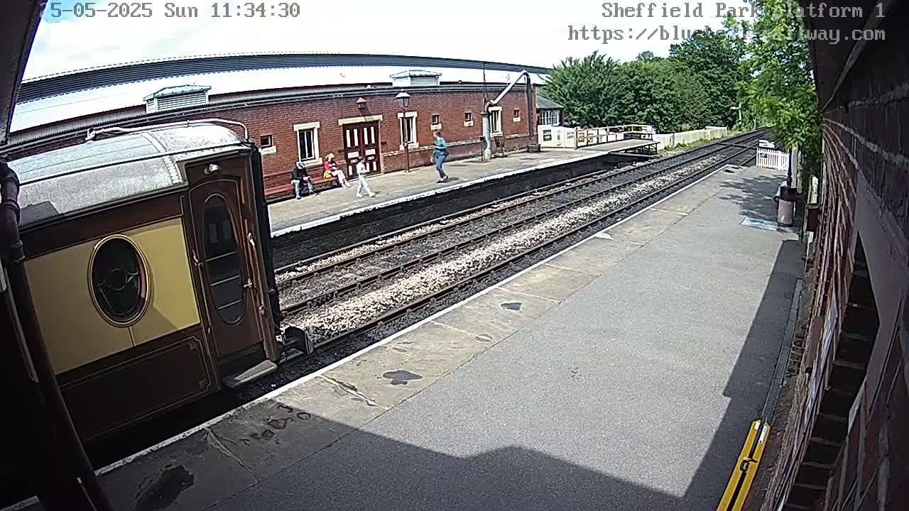 A partly sunny day shows a train car at a train station platform with a few people standing nearby.