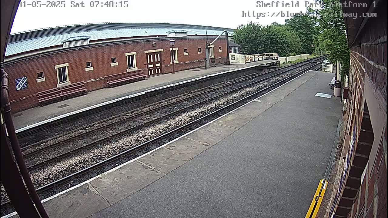 A brick train station platform with two sets of train tracks under an overcast sky.