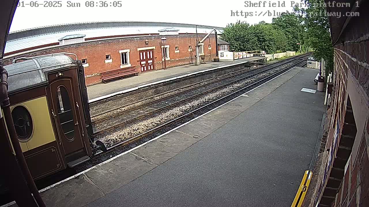 A vintage train car sits at a railway platform on an overcast day next to a brick building.