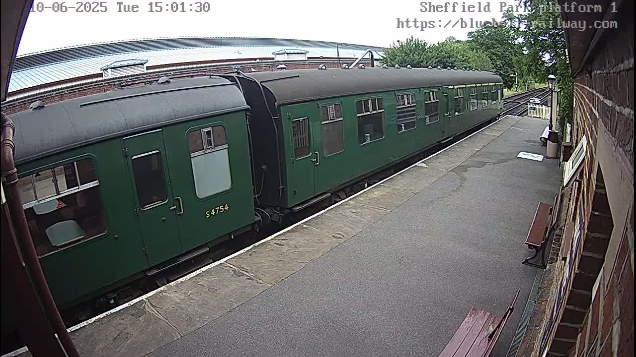 A long green train is at a station platform on an overcast day.