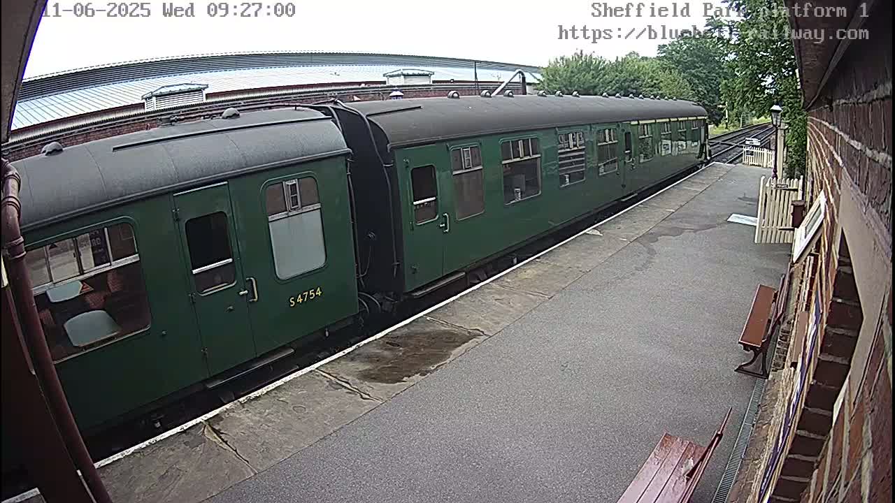 A long, dark-green passenger train sits at a station platform on an overcast day.