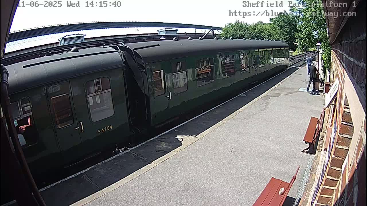A dark green passenger train is stopped at a station on a sunny day.