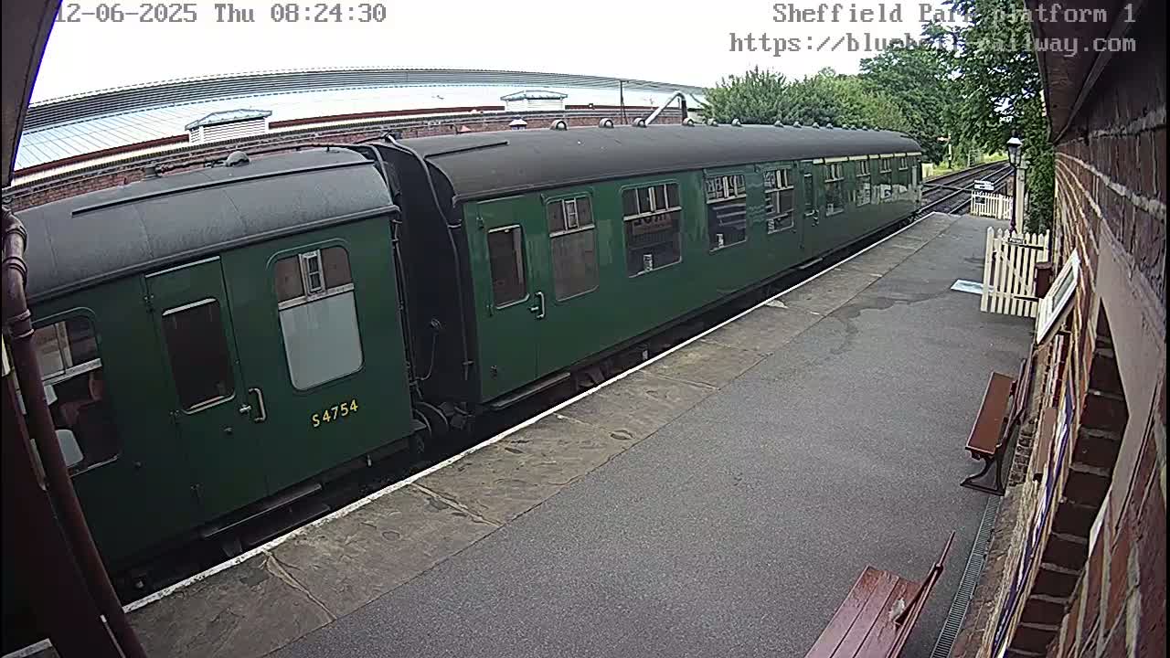 A long, dark-green train car sits at a station platform on an overcast day.