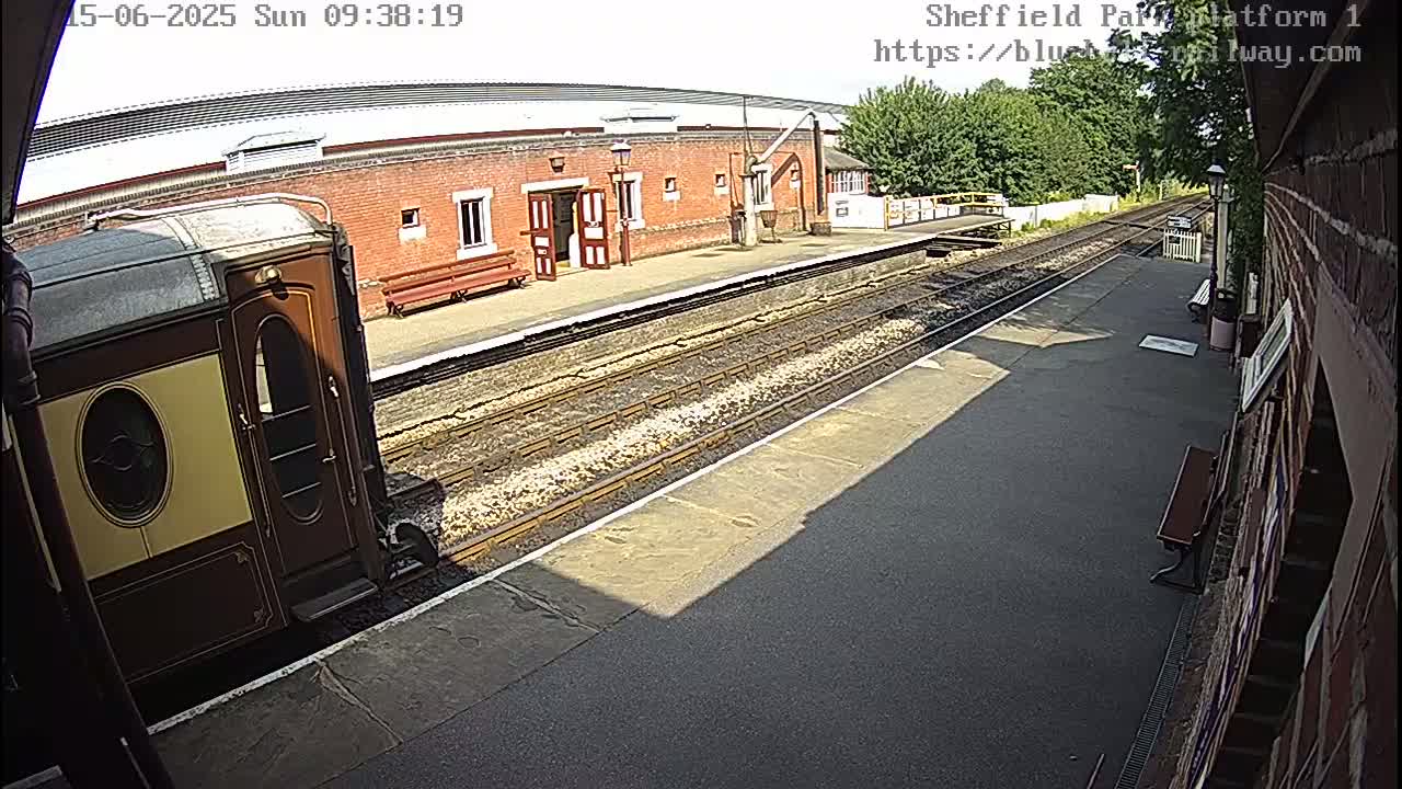 A vintage train car sits at a sunny train station platform next to a brick building.