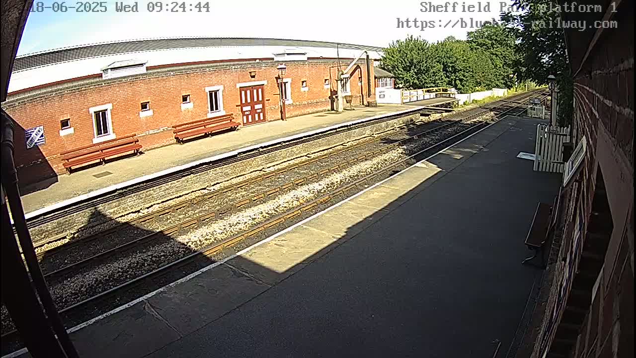 A sunny view of a train platform with a brick building and train tracks.